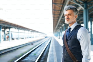 Guapo hombre de negocios maduro en una ciudad. Hombre esperando el tren en la estación de tren.