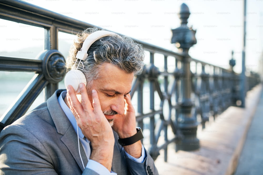 Handsome mature businessman with headphones in a city. Man sitting on a bridge, listening to music.