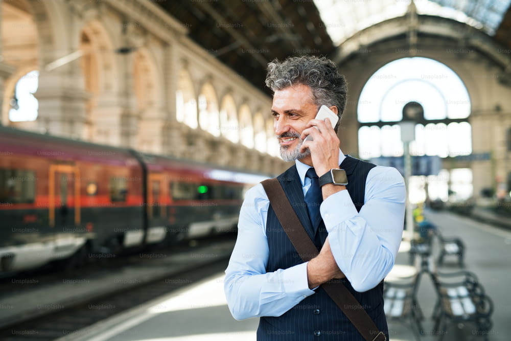 街でスマートフォンを持つハンサムな成熟した実業家。駅で電車を待っていて、電話をかける男。