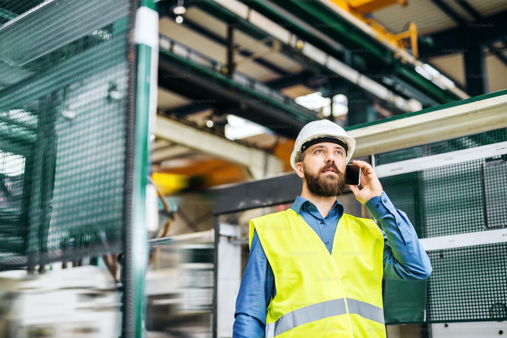 A portrait of a mature industrial man engineer with smartphone working in a factory, making a phone call.