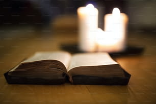 Primo piano di una vecchia Bibbia posata sul pavimento di legno, candele accese accanto ad essa