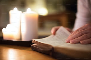 Donna irriconoscibile sdraiata sul pavimento a leggere la sua Bibbia. Candele accese accanto a lei. Primo piano del libro e della sua mano.
