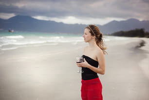 Beautiful woman with glass of red wine is relaxing and enjoying the sea view at the sandy beach