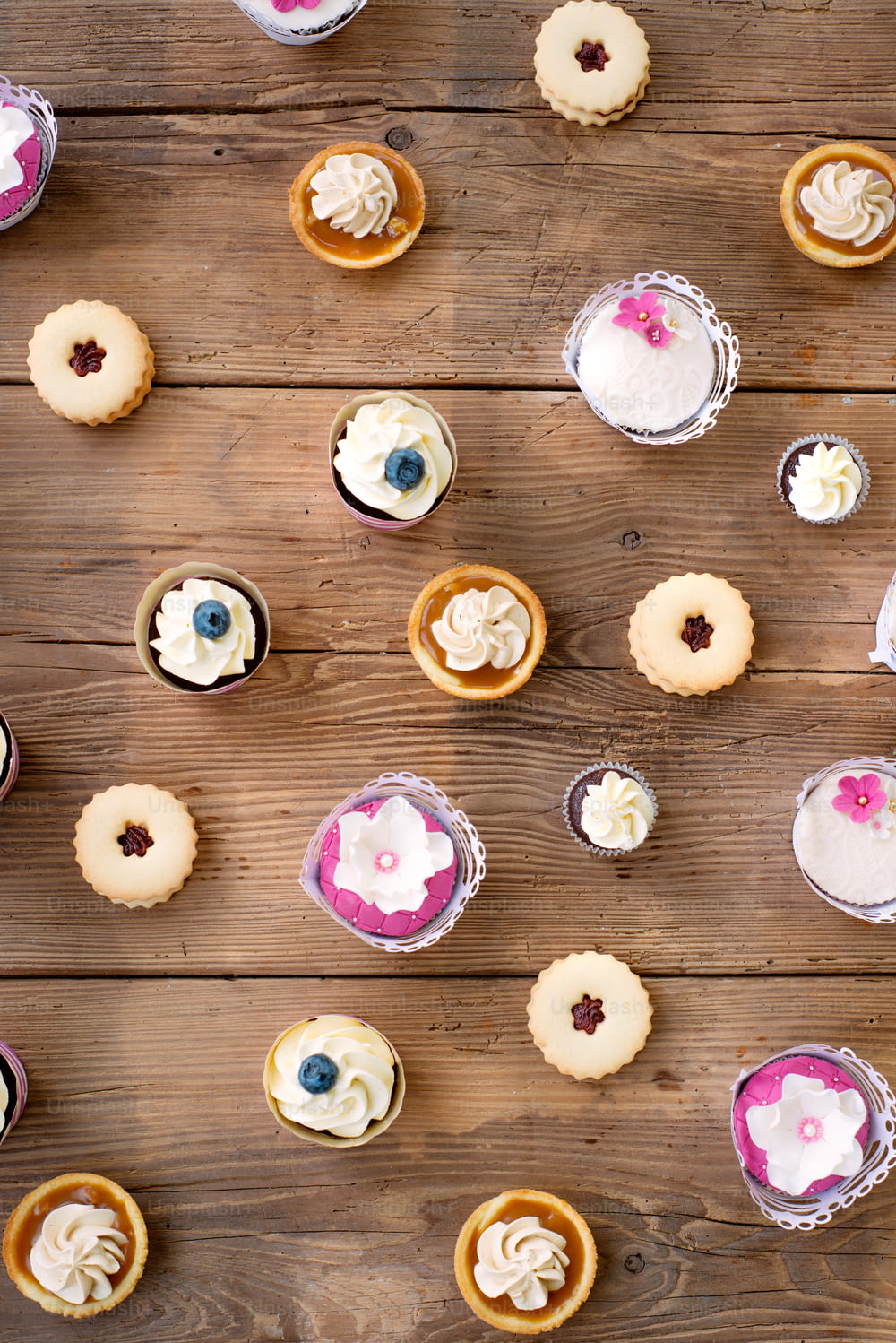Table with various cupcakes, tarts and cookies. Studio shot on brown wooden background. Flat lay.