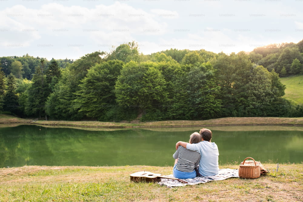 Schönes älteres Paar am See bei einem Picknick. Grüne, sonnige Sommernatur.