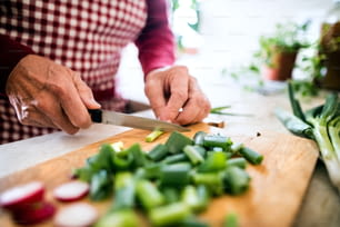 Personne âgée méconnaissable préparant de la nourriture dans la cuisine. Un vieil homme coupant des légumes.