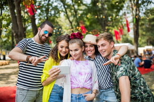 Front view of group of young friends with smartphone at summer festival, taking selfie.