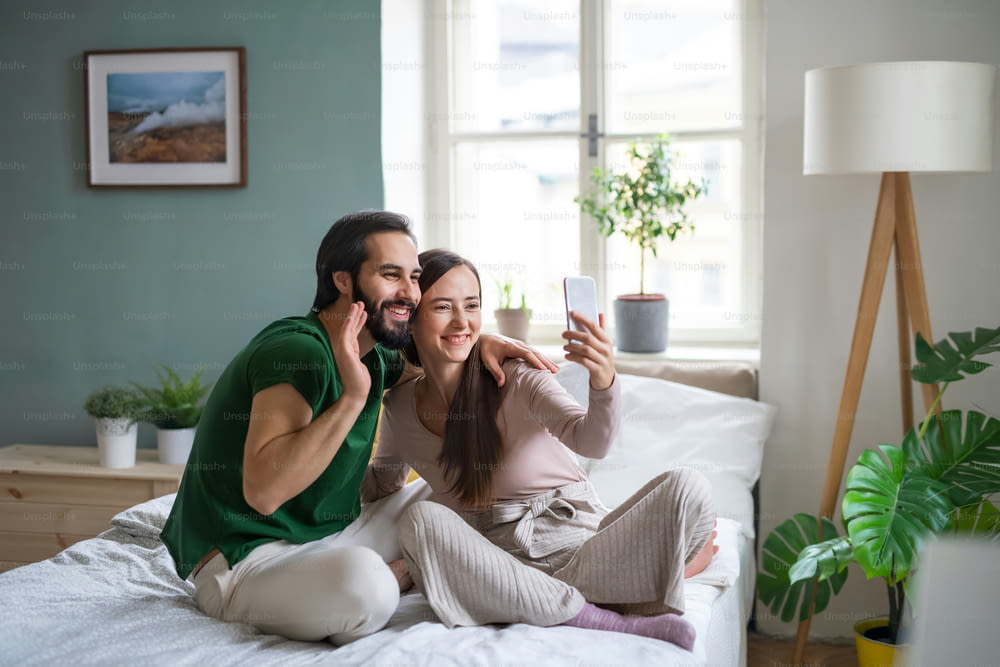Happy young couple taking selfie on bed indoors at home.