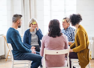 Hommes et femmes assis en cercle pendant la thérapie de groupe, notes adhésives avec des émotions négatives sur le front.