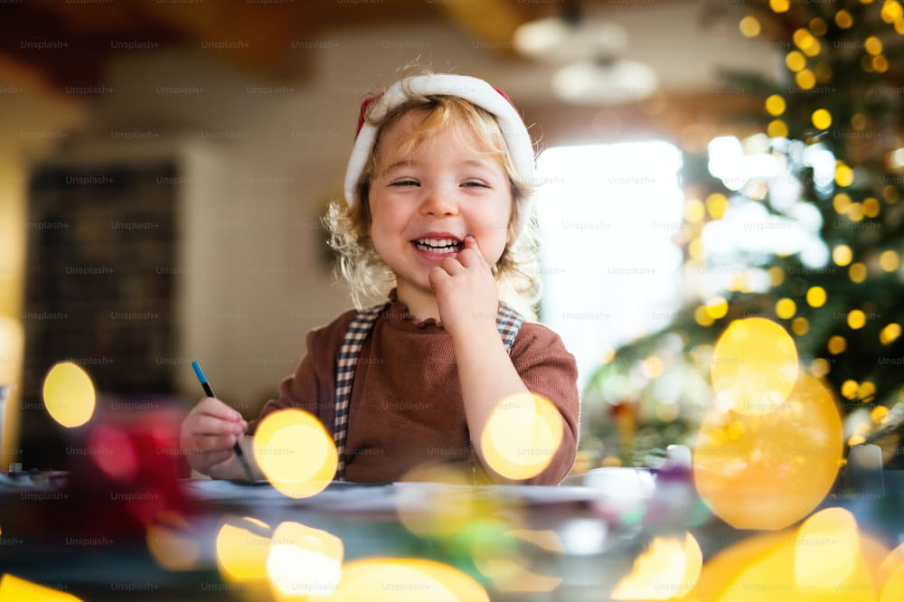 Porträt eines glücklichen kleinen Mädchens, das zu Weihnachten zu Hause ist und Bilder malt.