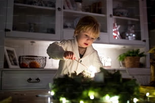 クリスマスに自宅の屋内にいる小さな男の子のポートレート、花輪に稲妻のろうそく。