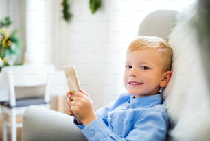 Un ragazzino con lo smartphone seduto su una poltrona di casa nel periodo natalizio, che gioca.