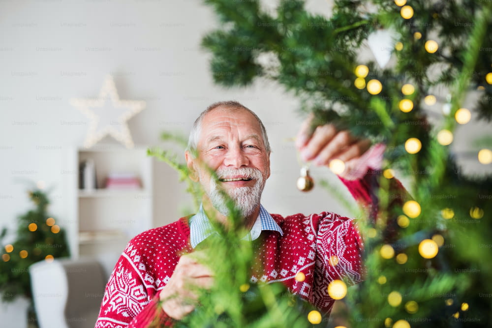 A cheerful senior man standing by Christmas tree, holding balls ornaments.