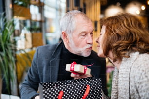 Couple de personnes âgées faisant des achats de Noël. Un homme offrant un cadeau à une femme. Centre commercial au moment de Noël.