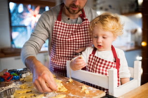 Unrecognizable man and toddler boy making cookies at home. Father and son baking gingerbread Christmas cookies.