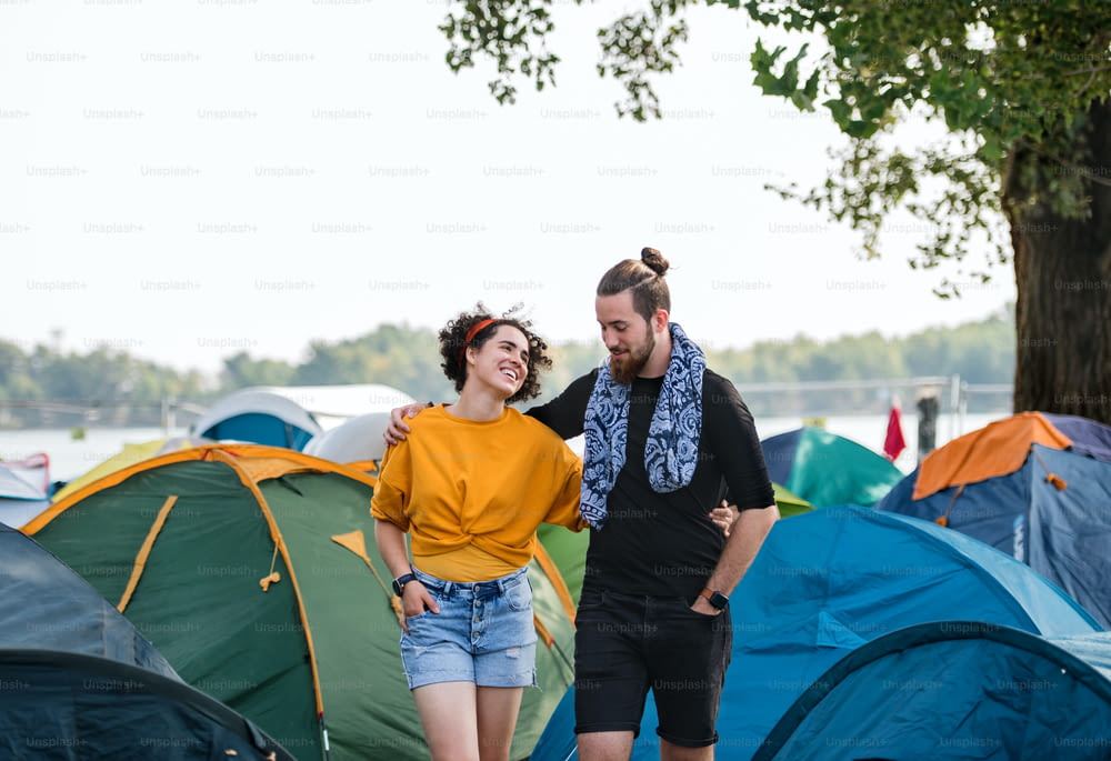 Jeune couple en vacances, marchant bras dessus bras dessous parmi les tentes.