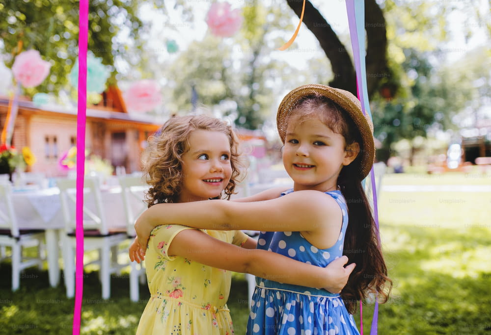 Small girls hugging outdoors in garden in summer, a birthday celebration concept.