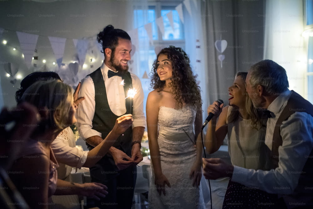 A young cheerful bride and groom with other guests dancing and singing on a wedding reception.