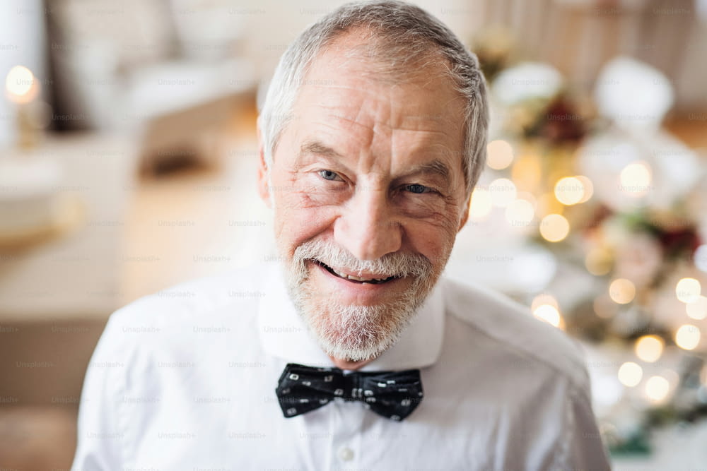A close-up portrait of a senior man with gray beard and mustache standing indoors in a room set for a party.