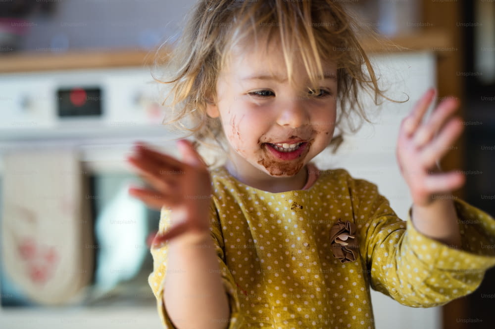 Fröhliches kleines Mädchen mit schmutzigem Mund drinnen in der Küche zu Hause, klatscht.