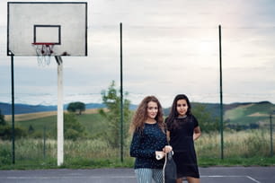 Deux adolescentes attrayantes à l’extérieur sur une aire de jeux avec planche à roulettes.