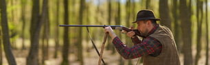 Una vista laterale dell'uomo cacciatore che mira con il fucile sulla preda nella foresta.