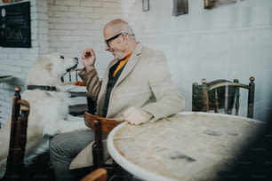 Un anciano feliz sentado en la cafetería y jugando con su perro, disparó a través del vidrio.
