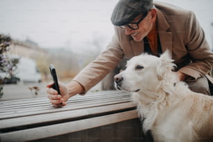 ベンチに座って、街の屋外で犬と一緒に自分撮りをする幸せな年配の男性。