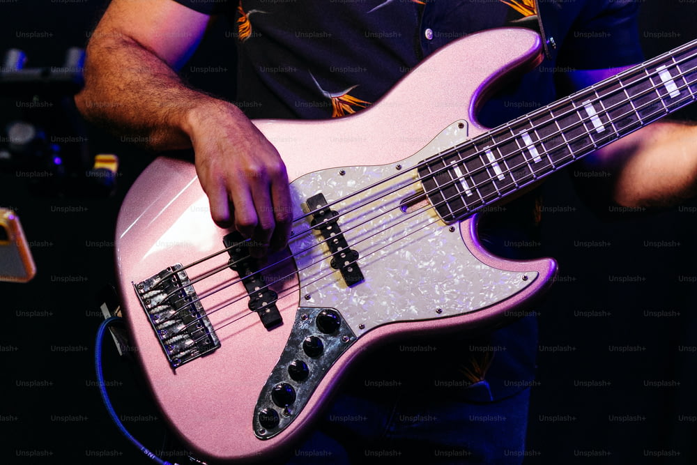男がピンクのベースギターを弾いている