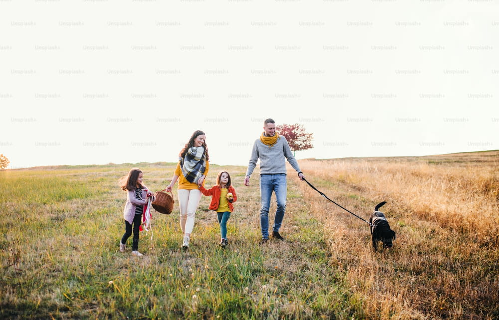 Una familia joven con dos niños pequeños y un perro negro en un paseo por la naturaleza otoñal.