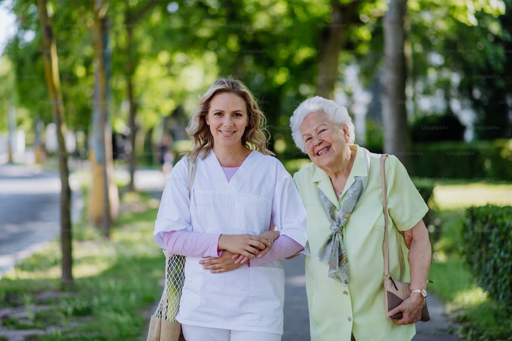 Portrait of caregiver with senior woman on walk in park.