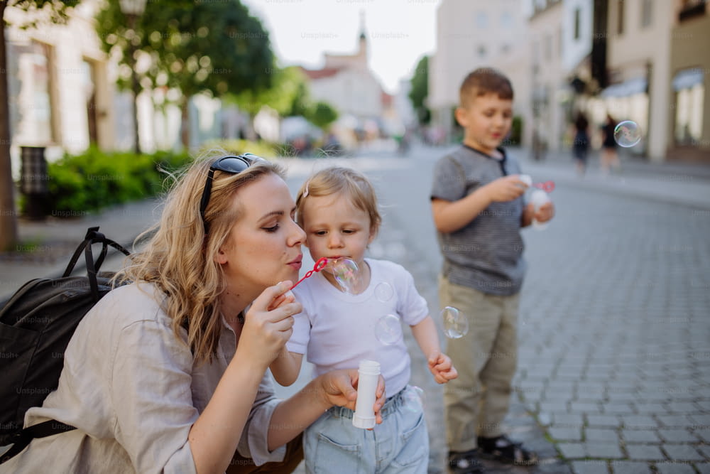 A young mother playing with her kids, blowing bubbles in city street in summer.