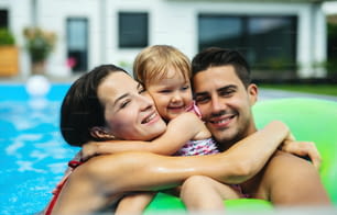 Familia joven feliz con hija pequeña en piscina al aire libre en el jardín del patio trasero.