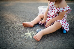 Sección media de una niña irreconocible al aire libre en el campo, dibujo de tiza en la carretera.