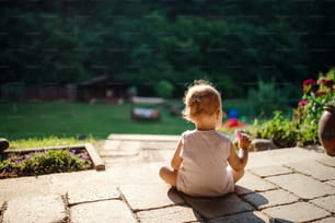 Una vista trasera de una niña sentada al aire libre en el patio en verano, dibujo de tiza.