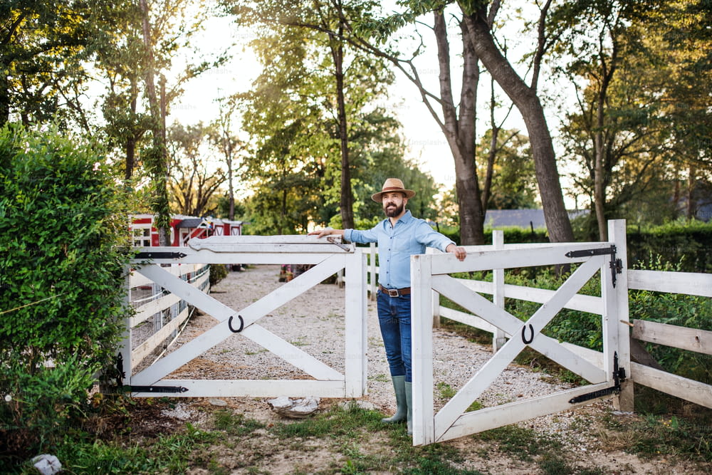 Un ritratto di agricoltore maturo che cammina all'aperto nella fattoria di famiglia, aprendo il cancello.