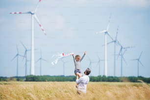 Mature father with small daughter standing on field on wind farm, playing.