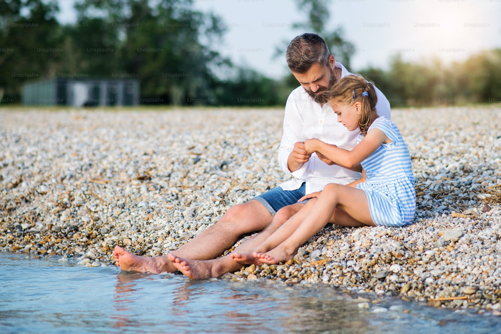 아버지와 작은 딸이 호수나 바다 옆에 앉아 휴가를 보내는 모습.