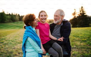 Ein aktives älteres Paar mit fröhlicher Enkelin, die bei Sonnenuntergang in der Natur steht.