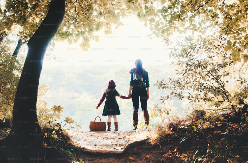 가을 자연의 숲에 서 있는 어린 딸과 함께 손을 잡고 있는 어머니의 뒷모습.