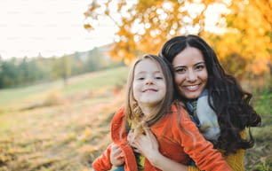 A portrait of young mother with a small daughter sitting in autumn nature at sunset.