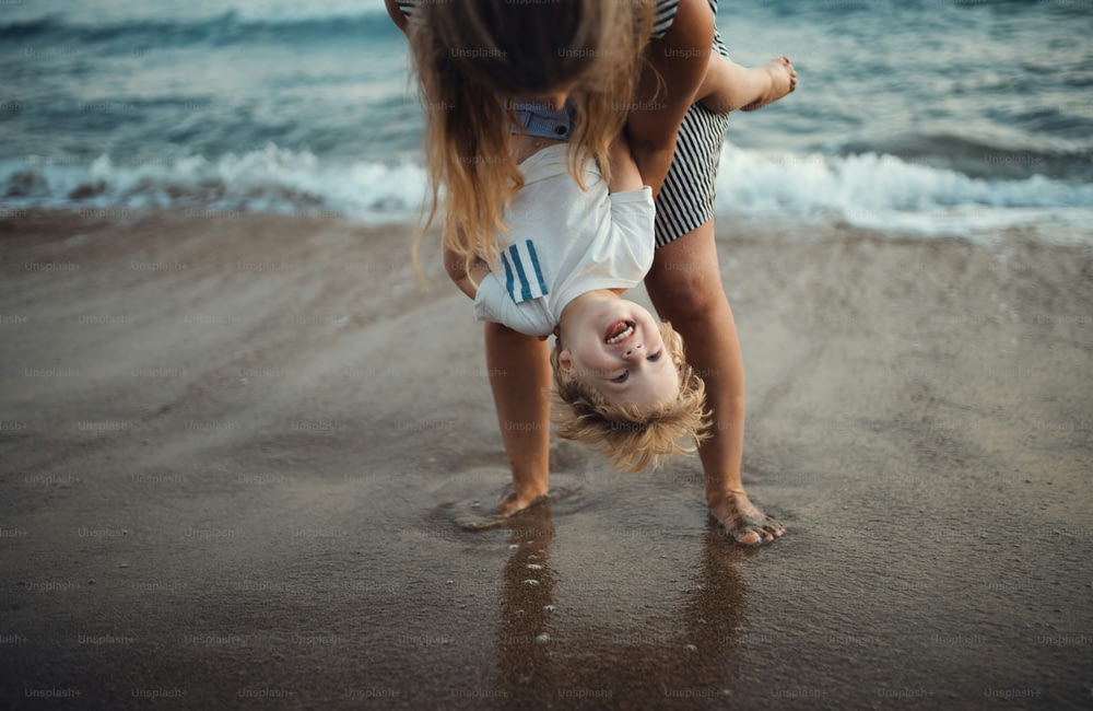 Une jeune mère avec un enfant en bas âge debout sur la plage pendant les vacances d’été, s’amusant.