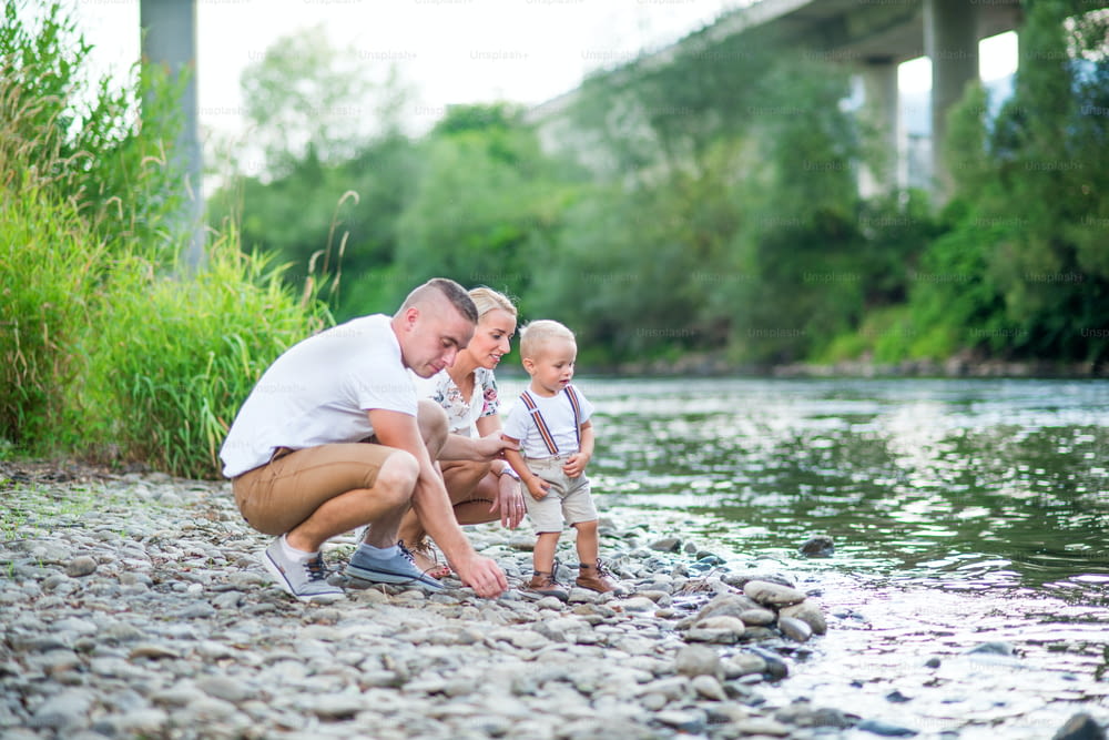Familia joven con un niño pequeño que pasa tiempo en la naturaleza soleada del verano, jugando junto al río.