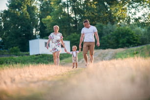 Familia joven con un niño pequeño caminando en la naturaleza soleada del verano, tomados de la mano.