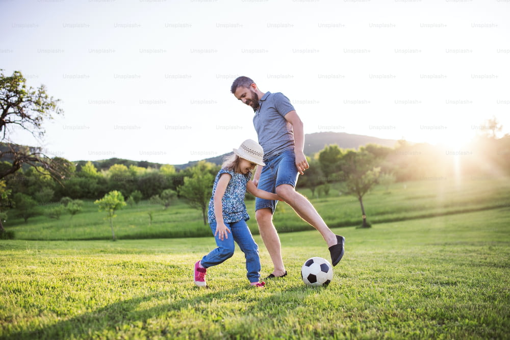 Pai com uma filha pequena brincando com uma bola na natureza ensolarada da primavera.