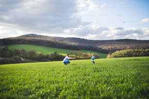 Un padre maduro con su hijo pequeño corriendo afuera en la naturaleza verde y soleada de primavera.