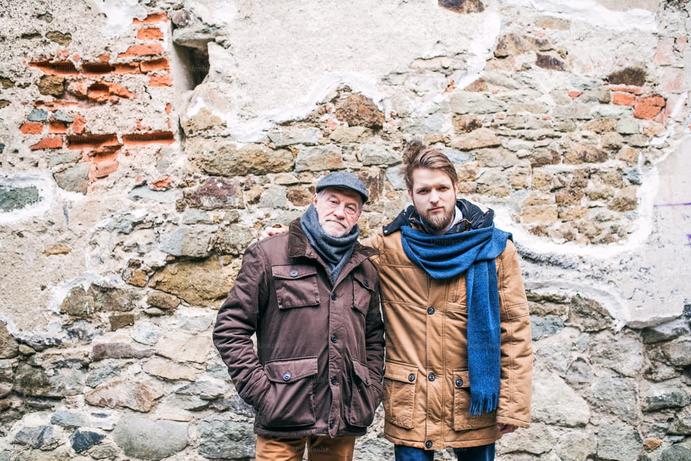 Älterer Vater und sein kleiner Sohn bei einem Spaziergang in der Stadt. Zwei Männer stehen an einer alten Backsteinmauer.