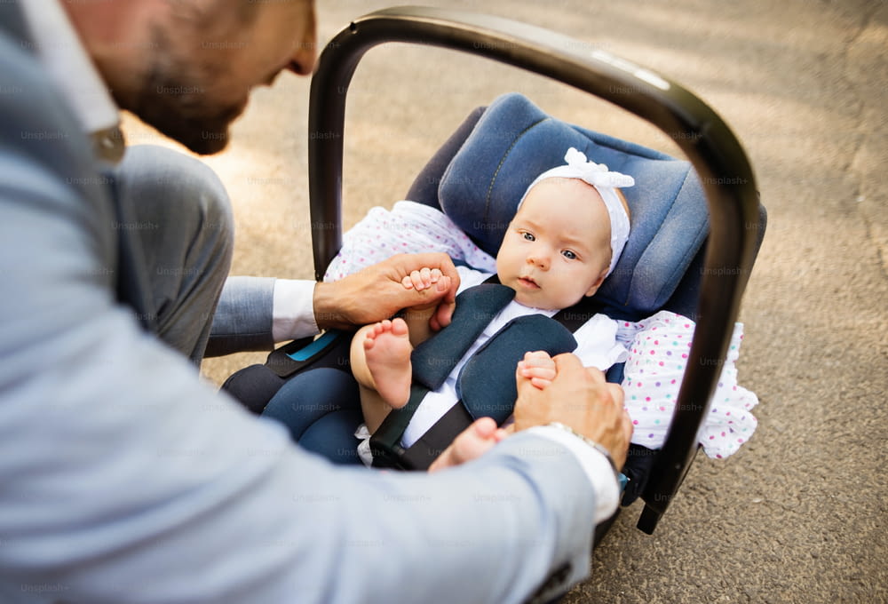 Unrecognizable father outdoors with his cute baby daughter sitting in car safety seat.