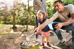 Bella famiglia che si gode le vacanze in campeggio nella foresta. Padre che cucina carne sulla griglia del barbecue.