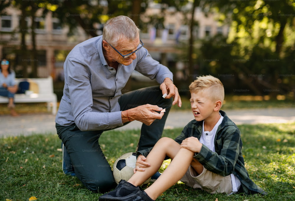 Un ragazzino con la gamba ferita che piange, suo nonno gli sta dando il gesso all'aperto nel parco.